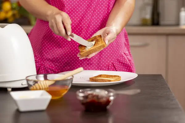 Kadın ellerinin kızarmış ekmek diliminin üzerine tereyağı sürdüğü ve kahvaltı için sandviç hazırladığı ayrıntılar. Bıçak ve ellere odaklan.