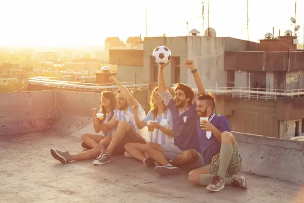 ビルの屋上でサッカーの試合を見ている若い友人のグループ 応援し ビールを飲む 右側の男性に焦点を当てる — ストック写真