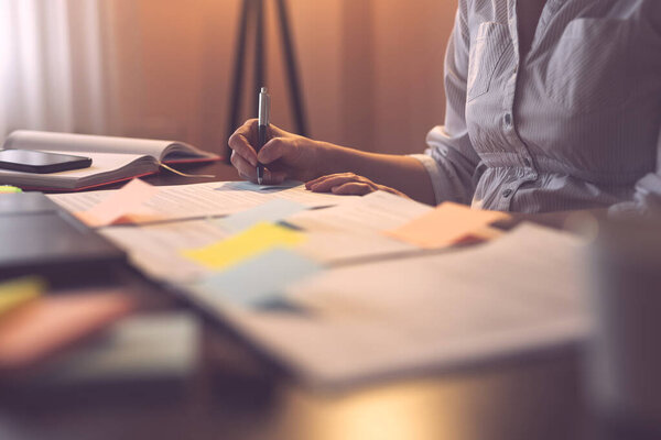 Деталь женской руки при подписании контракта; деловая женщина, работающая в домашнем офисе. Сосредоточься на ручке и пальцах