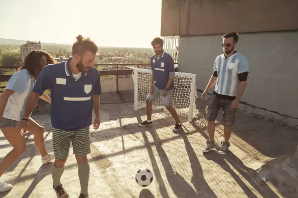 Group of people wearing jerseys having fun playing football on a building rooftop terrace on a sunny summer day
