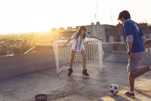Couple in love wearing jerseys, playing football on a building rooftop.