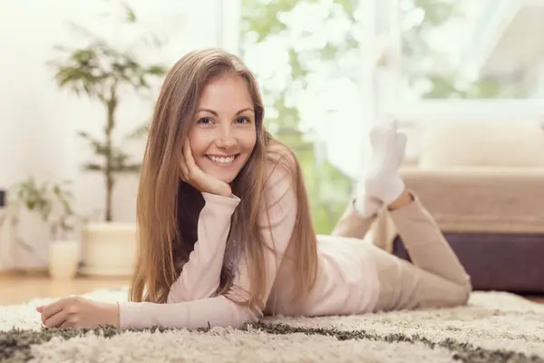 Beautiful brunette lying on the carpet on the floor of her apartment, enjoying her leisure time