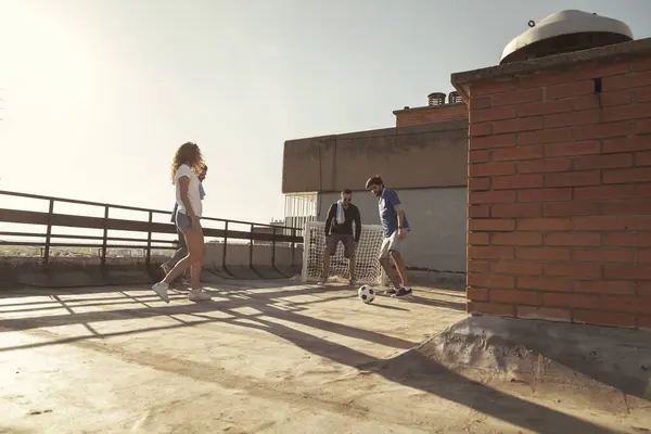 Low angle view of group of young friends having fun playing football on a building rooftop terrace on a sunny summer day