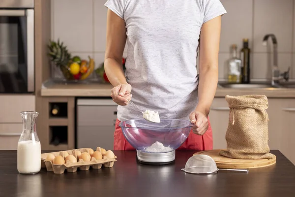 Un ölçmek için mutfak terazisi kullanan kadın ellerinin ayrıntıları; kek yapmak için malzeme ölçen, çuval bezinden kaşıkla un alan kadın