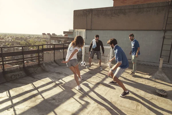 Young friends wearing jerseys having fun playing football on a building rooftop terrace on a sunny summer day, warming up before the game