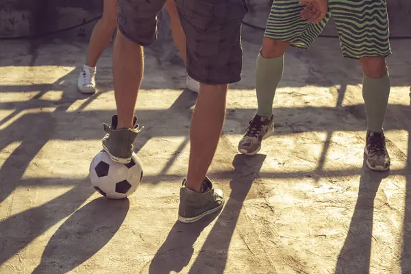 Detail of group of young friends having fun playing football on a building rooftop terrace on a sunny summer day, close up of the legs and the ball