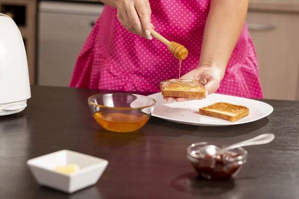 トーストパンのスライスと木のスプーンを持っている女性の手の詳細 パンの上に蜂蜜を広める 女性は朝食のためのバターと蜂蜜サンドイッチを作る — ストック写真