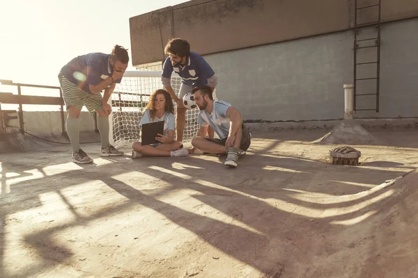 Group of young friends having fun playing a football match on a building rooftop terrace, taking a time out, planning the game strategy and drawing it on the board