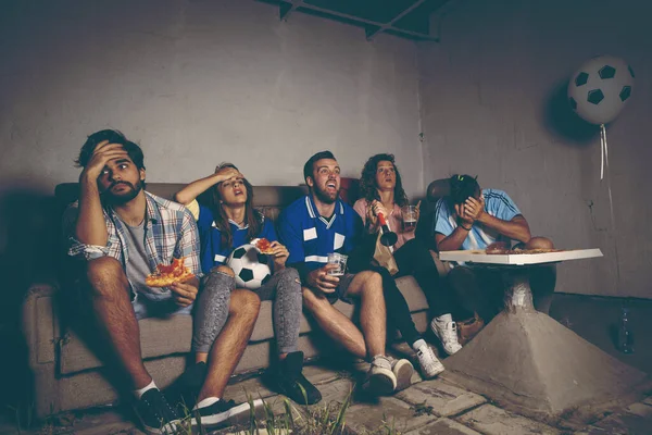 Group of young friends watching a football match on a building rooftop, cheering eating pizza and drinking beer, disappointed after they lost the match