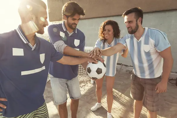 Group of young friends having fun playing football on a building rooftop terrace, holding the ball before the match; football fans holding soccer ball all together before the game