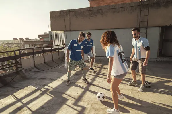 Group of friends wearing jerseys having fun playing football on a building rooftop terrace on a sunny summer day