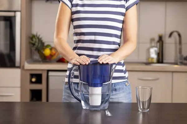 Detail of female hands holding a filtered water pitcher, waiting for the water to be filtered after filling the pitcher with a tap water