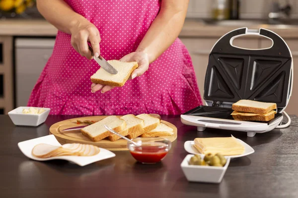 Ekmek dilimine tereyağı süren kadın elleri kahvaltıda sandviç makinesinde sıcak sandviç yapan kadın.