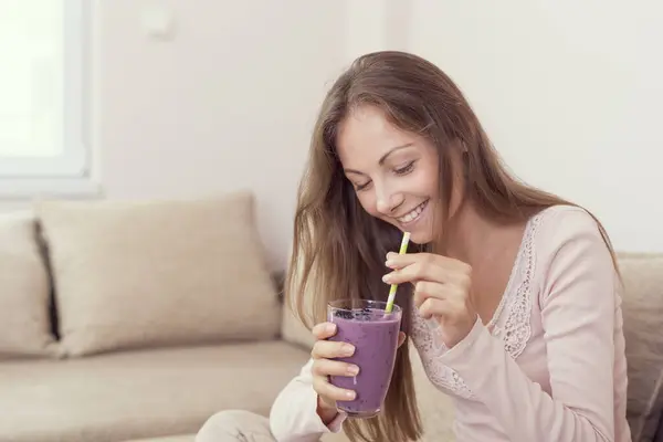 漂亮的姑娘坐在客厅的沙发上 面带微笑 手里拿着一杯覆盆子和蓝莓调匀的软糖 — 图库照片