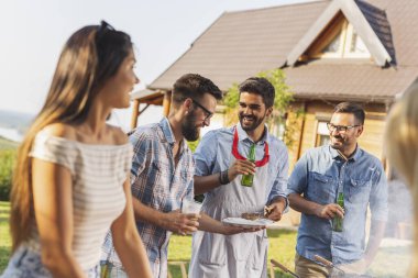 Bir grup arkadaş arka bahçede barbekü yapıyor, bira içiyor ve güneşli bir yaz gününde eğleniyorlar.