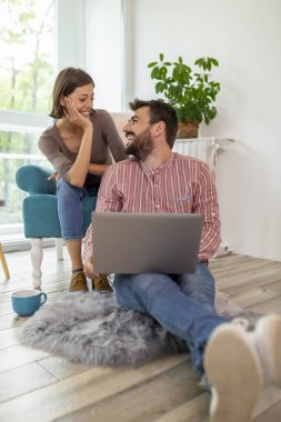 Birbirini seven bir çift evde rahatlıyor, kahve içiyor ve internette dizüstü bilgisayarla geziniyor, birlikte boş zamanlarının tadını çıkarıyor.