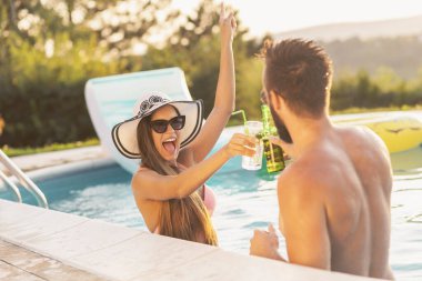 Havuz başında bir yaz partisinde aşık bir çift havuz kenarında suyun içinde durup kadeh kaldırıyor.