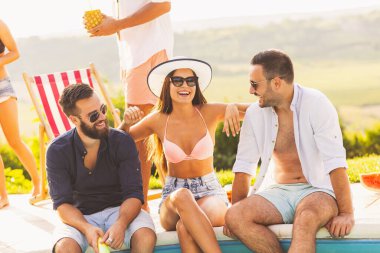 Havuz başında bir yaz partisinde bir grup arkadaş yüzme havuzunun kenarında oturuyor, kokteyl içiyor ve eğleniyorlar.