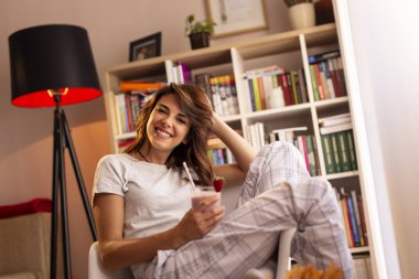 Güzel bir genç bayan hafta sonu sabahının tadını çıkarıyor, kahvaltı yapıyor ve taze çilekli smoothie içiyor.