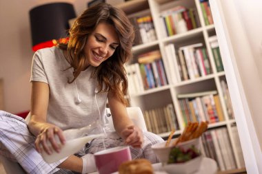 Güzel genç bir kadın kahvaltı gevreğine süt dolduruyor.