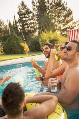Havuz başında bir yaz partisinde bir grup arkadaş yüzme havuzunda eğleniyor, bira içiyor ve su sıçratıyor.