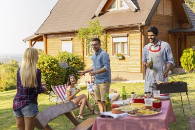 Bir grup arkadaş arka bahçede barbekü partisi veriyor, et pişiriyor, bira içiyor, badminton oynuyor ve güneşli bir yaz gününde eğleniyorlar. Badminton oynayan adama odaklan.