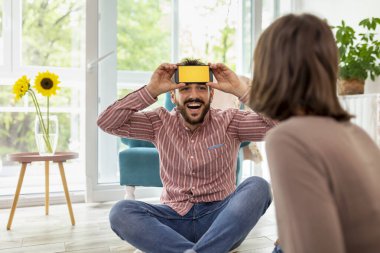 Çift evde sessiz sinema oynayarak eğleniyor, akıllı telefon uygulamasından gelen kelimeleri açıklıyor ve tahmin ediyor.