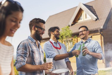 Bir grup arkadaş arka bahçede barbekü yapıyor, bira içiyor ve güneşli bir yaz gününde eğleniyorlar.