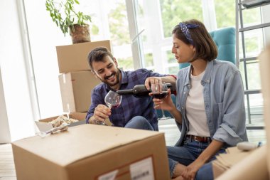 Yeni bir daireye taşınıp bir şişe şarap açıp kadeh kaldırarak kutlama yapan genç ve güzel bir çift.