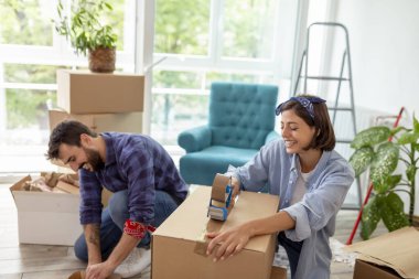 Güzel genç bir kadın ambalaj makinesi kullanıyor, karton kutuları kaydediyor, taşınmaya hazırlanıyor, taşınırken eşyalar paketleniyor.