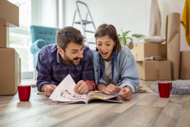 Birbirine aşık bir çift yeni evlerinin zemininde uzanıp ev dekorasyonu dergilerinde iç tasarım fikirleri arıyor ve kahve içiyor.