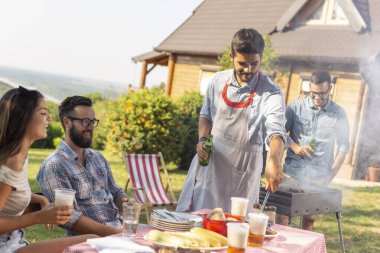 Bir grup arkadaş arka bahçede barbekü yapıyor, bira içiyor ve güneşli bir yaz gününde eğleniyorlar.