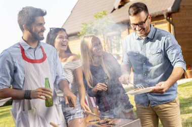 Bir grup arkadaş arka bahçede barbekü yapıyor, bira içiyor ve güneşli bir yaz gününde eğleniyorlar.