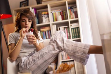 Güzel genç bayan hafta sonu sabahının tadını çıkarıyor, kahvaltı yapıyor ve taze çilekli smoothie içiyor.