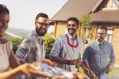 Bir grup arkadaş arka bahçede barbekü yapıyor, bira içiyor ve güneşli bir yaz gününde eğleniyorlar.
