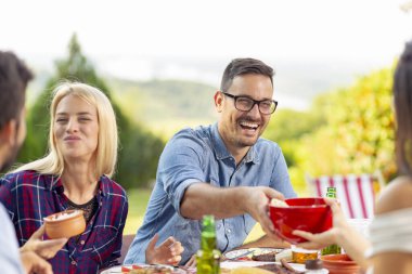 Bir grup arkadaş dışarıda barbekü yapıyor, ızgara et yiyor, bira içiyor ve eğleniyorlar.
