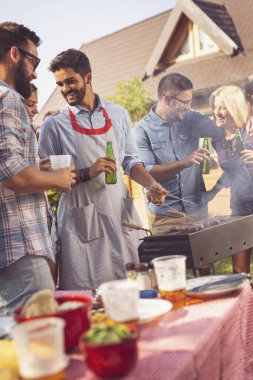 Bir grup arkadaş arka bahçede barbekü yapıyor, bira içiyor ve güneşli bir yaz gününde eğleniyorlar.