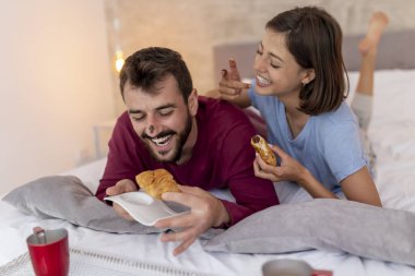 Birbirine aşık çiftler pijama giyer, sabah uyandıktan sonra yatakta kahvaltı ve kahve yaparlar.