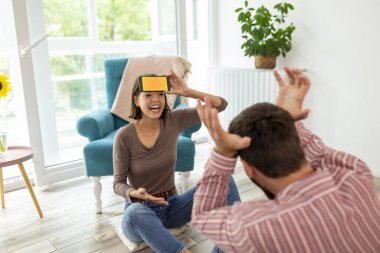 Çift evde sessiz sinema oynayarak eğleniyor, akıllı telefon uygulamasından gelen kelimeleri açıklıyor ve tahmin ediyor.