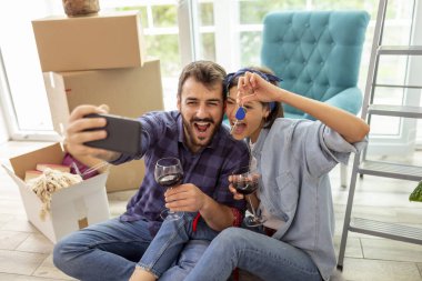 Genç çift yeni bir daireye taşınıyor, şarap içiyor ve ev anahtarlarıyla selfie çekerken eğleniyor.