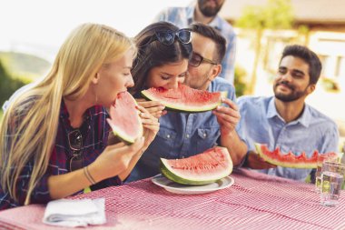 Bir grup arkadaş dışarıda öğle yemeği yiyor, taze karpuz dilimleri yiyor ve eğleniyorlar.