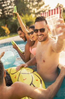 Havuz başında bir yaz partisinde bir grup arkadaş, yüzme havuzunda eğleniyorlar, kokteyl ve bira içiyorlar ve kadeh kaldırıyorlar.