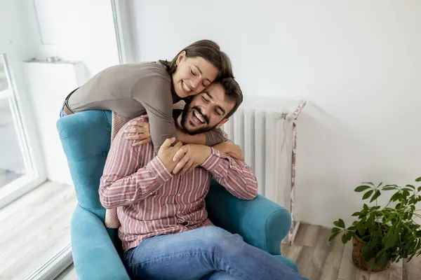 Couple in love sitting in an armchair by the window, hugging and enjoying their time together