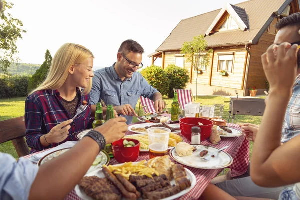 Bir grup arkadaş dışarıda barbekü yapıyor, ızgara et yiyor, bira içiyor ve eğleniyorlar.