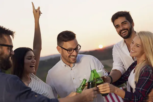 Group of friends at a summertime outdoor party having fun, dancing, drinking beer and making a toast
