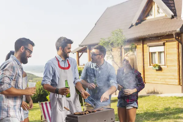 Bir grup arkadaş arka bahçede barbekü yapıyor, bira içiyor ve güneşli bir yaz gününde eğleniyorlar.