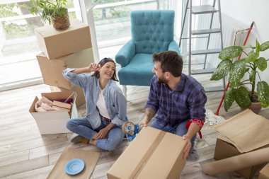 Aşık bir çift eşyalarını karton kutulara koyup taşınmaya hazırlanıyor. Erkek kutuları paketleme makinesiyle bantlarken kadın da kırılgan şeyleri kağıda sarıyor.