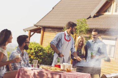 Bir grup arkadaş arka bahçede barbekü yapıyor, bira içiyor ve güneşli bir yaz gününde eğleniyorlar.