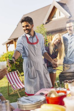 Bir grup arkadaş arka bahçede barbekü yapıyor, bira içiyor ve güneşli bir yaz gününde eğleniyorlar.
