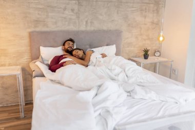 Güzel, genç ve aşık bir çift pijama giyip yatakta yatıyorlar ve sabahları sarılıyorlar.